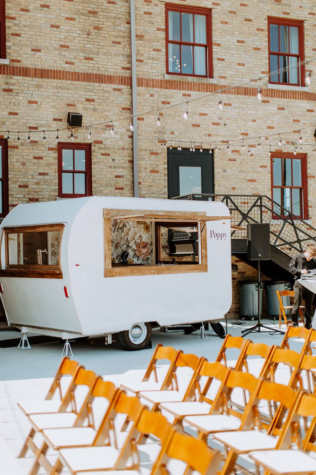 Vintage camper bar named Poppy set up in the 10 South courtyard next to ceremony seating and string lights in Janesville, WI