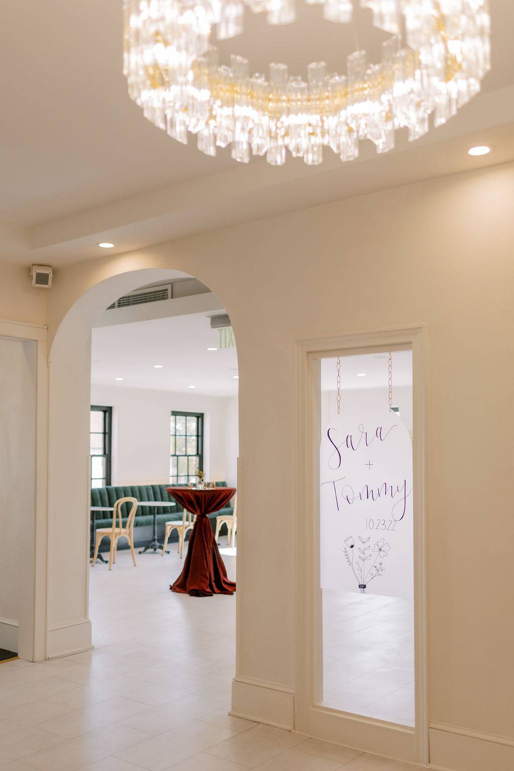 View through arched entry at 10 South showing velvet seating, custom welcome sign, and modern chandelier in Janesville, WI