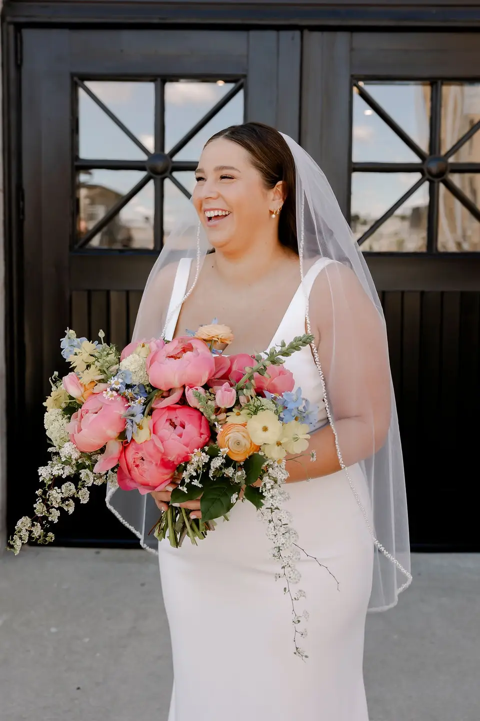 Smiling bride holding a vibrant bouquet outside 10 South wedding venue in Janesville, Wisconsin