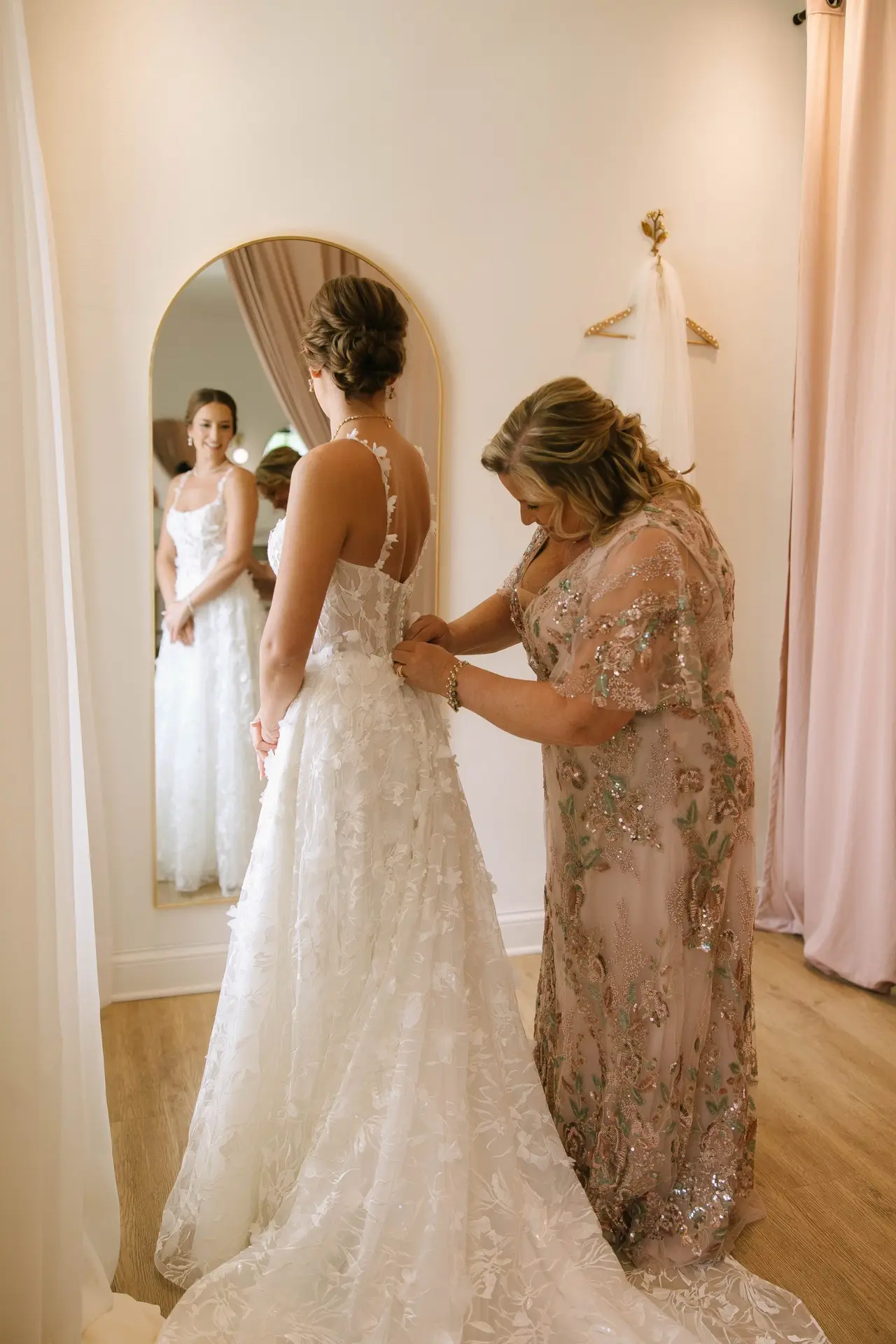 Mother helps bride zip her lace wedding gown in front of full-length mirror at 10 South’s bridal suite in Janesville, WI