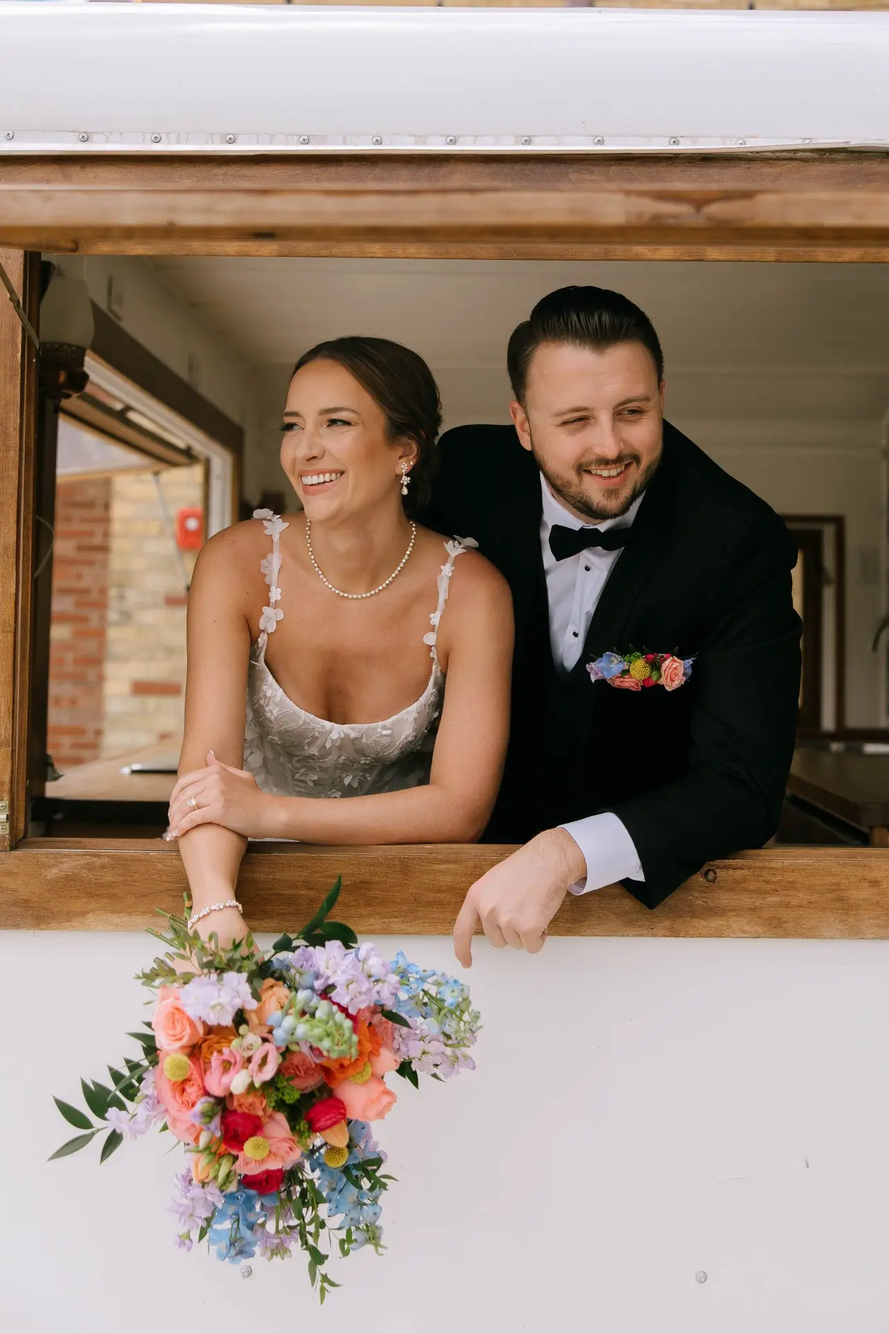 Bride and groom smile through the serving window of the Poppy camper bar at 10 South in Janesville, WI