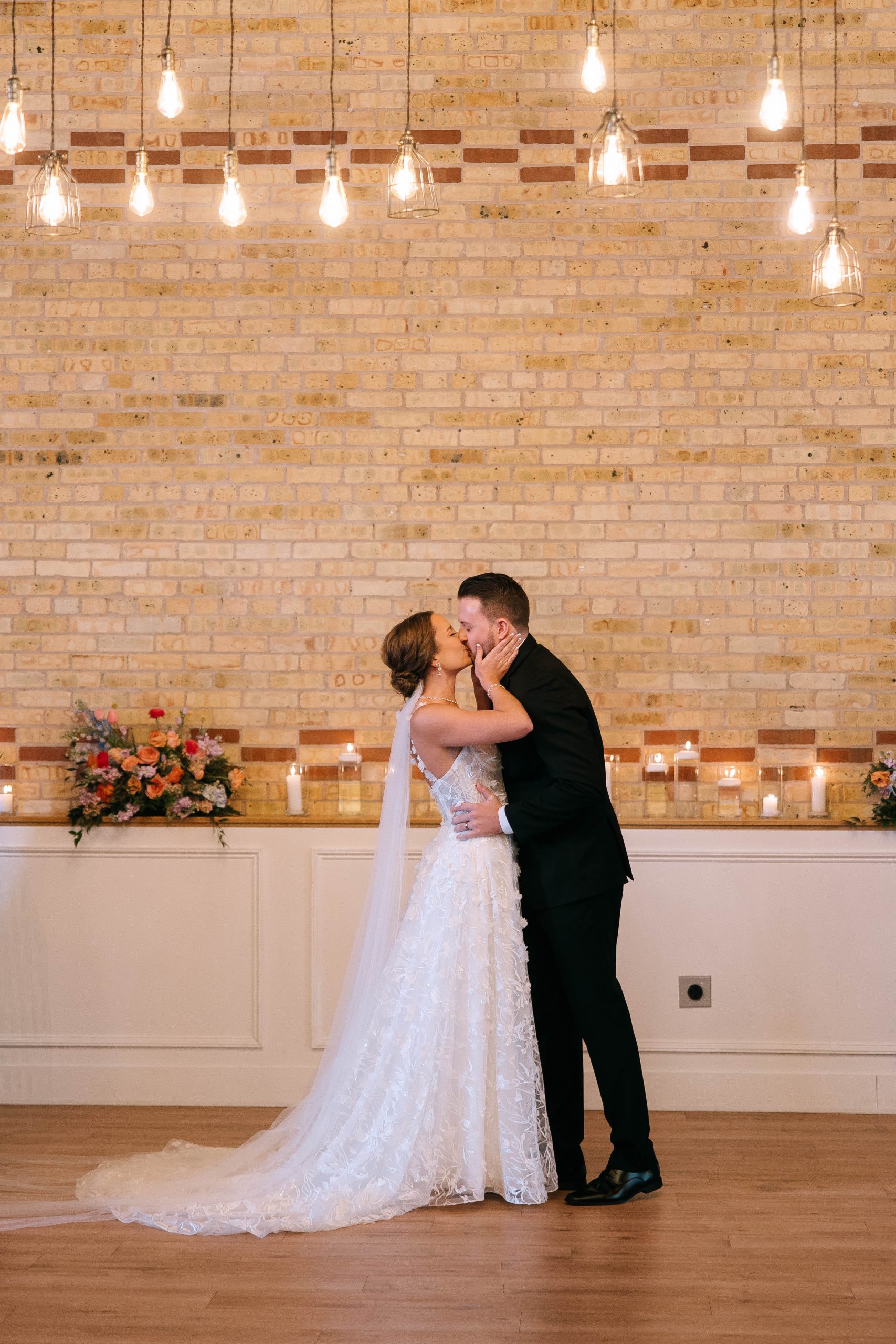 Bride and groom kiss during indoor wedding ceremony at 10 South with exposed brick backdrop and romantic candlelight.