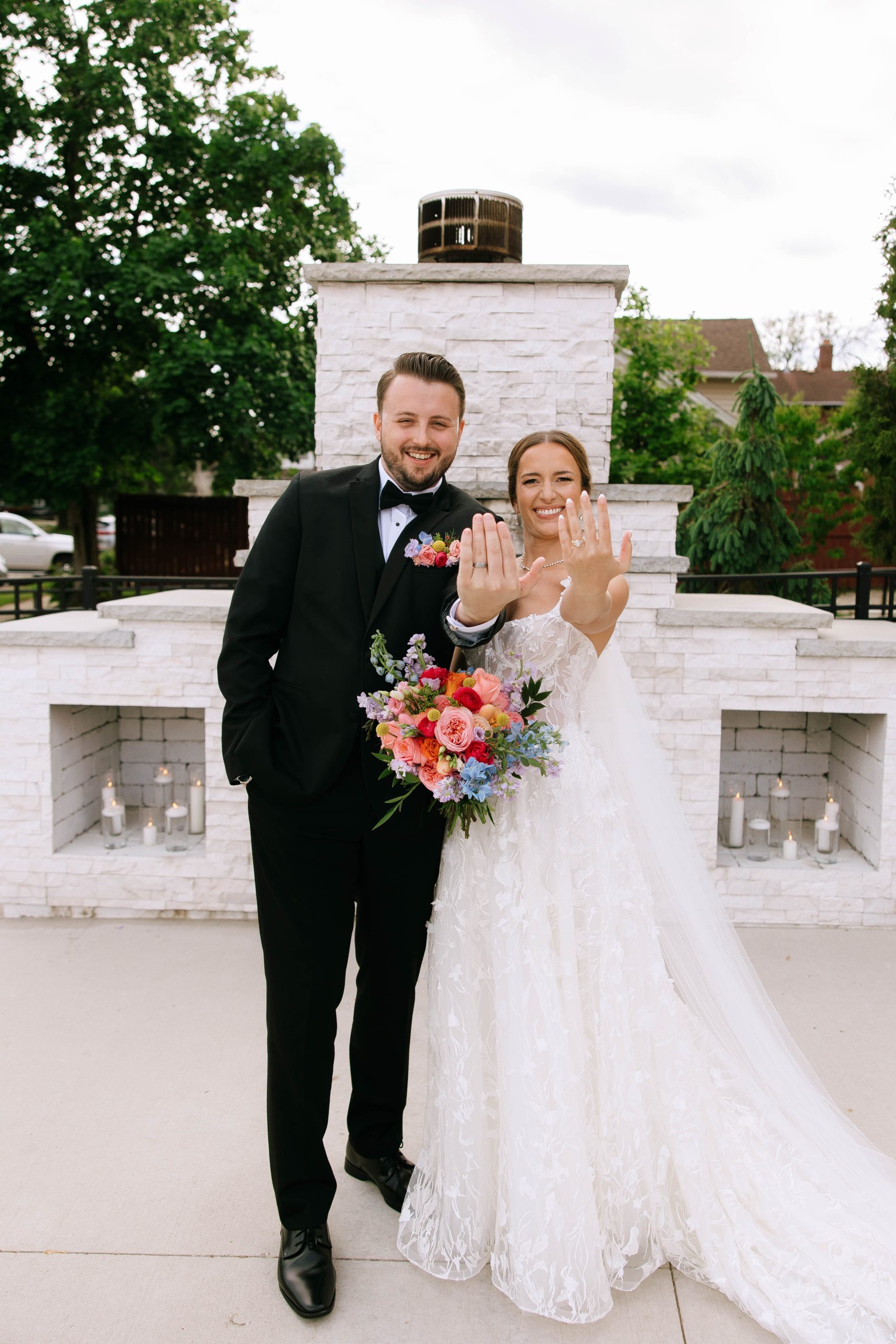 Just married couple showing off their wedding rings in front of the white stone fireplace at 10 South’s outdoor ceremony space.