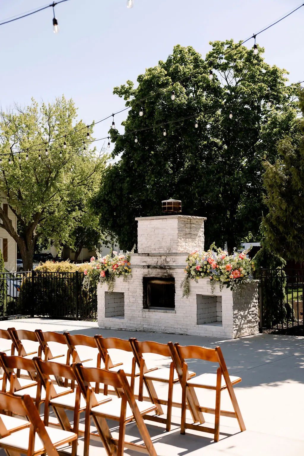 Outdoor wedding ceremony setup in front of white brick fireplace with floral arrangements at 10 South in Janesville, WI