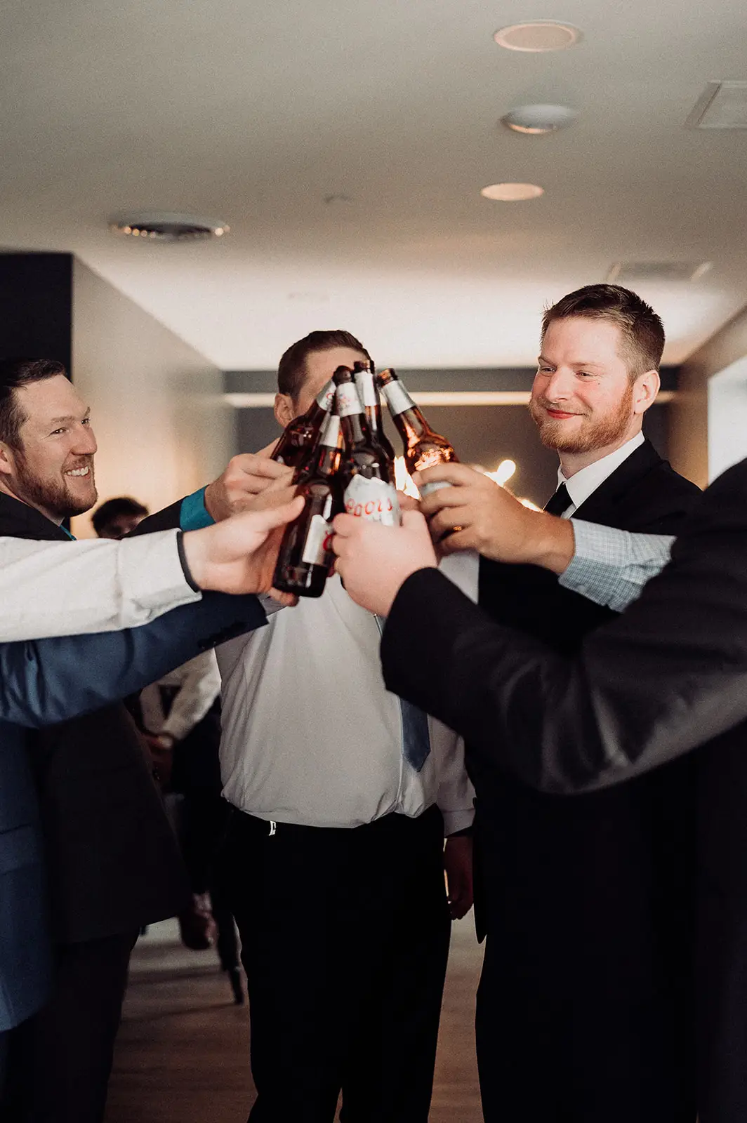 Groom and groomsmen raise beer bottles for a celebratory toast in the groom’s lounge at 10 South in Janesville, WI
