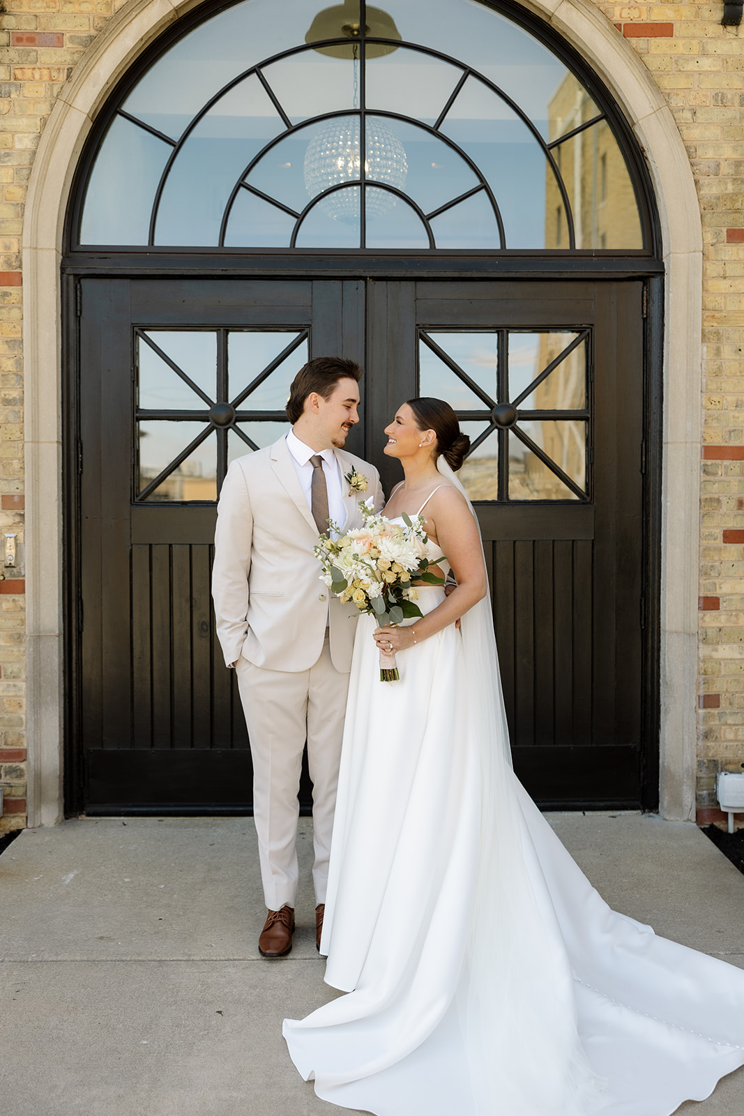 Bride and groom smiling at each other in front of the arched black double doors at 10 South wedding venue.