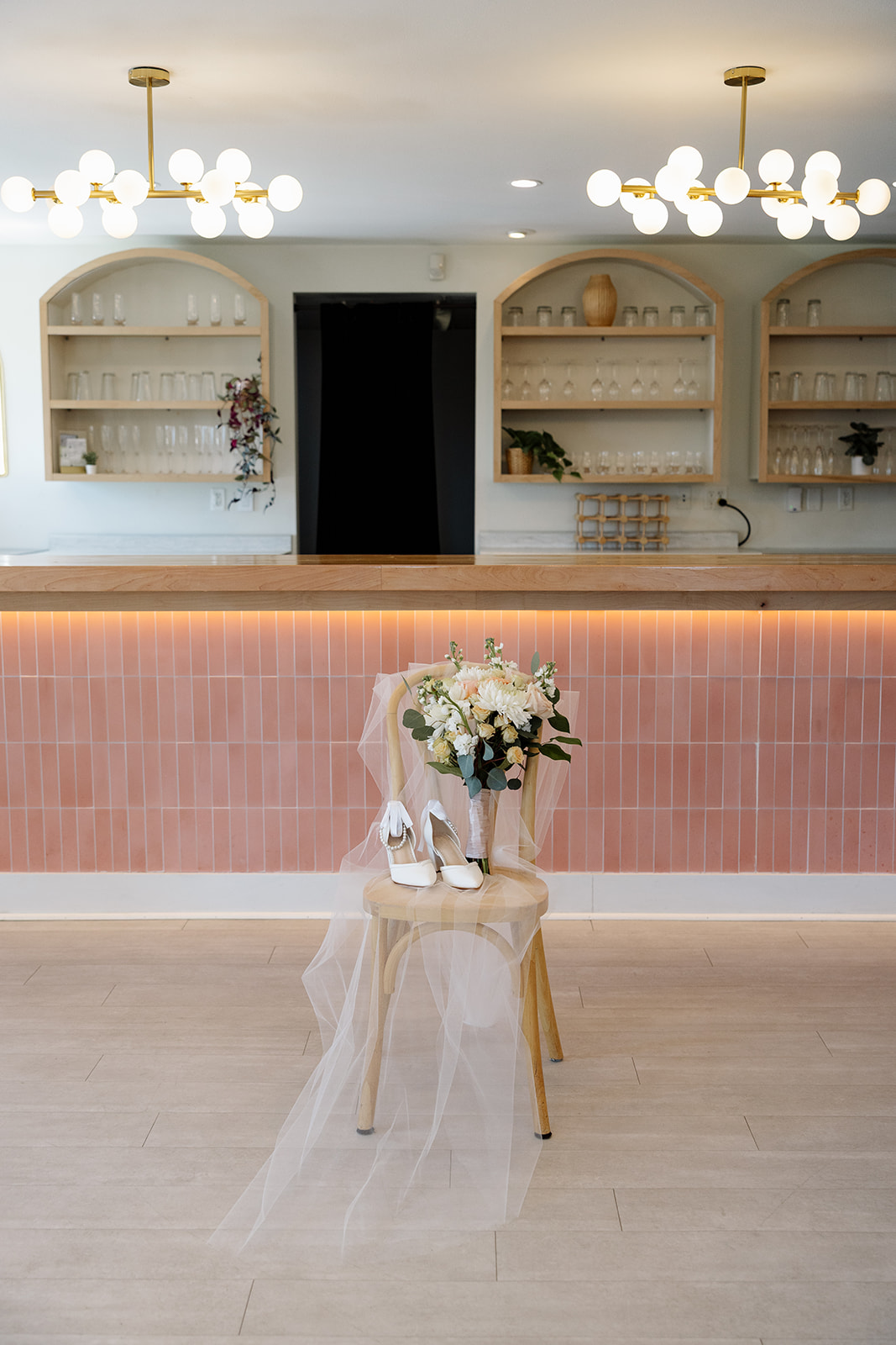 Bridal bouquet, veil, and heels displayed on a chair in front of the blush tile bar at 10 South.