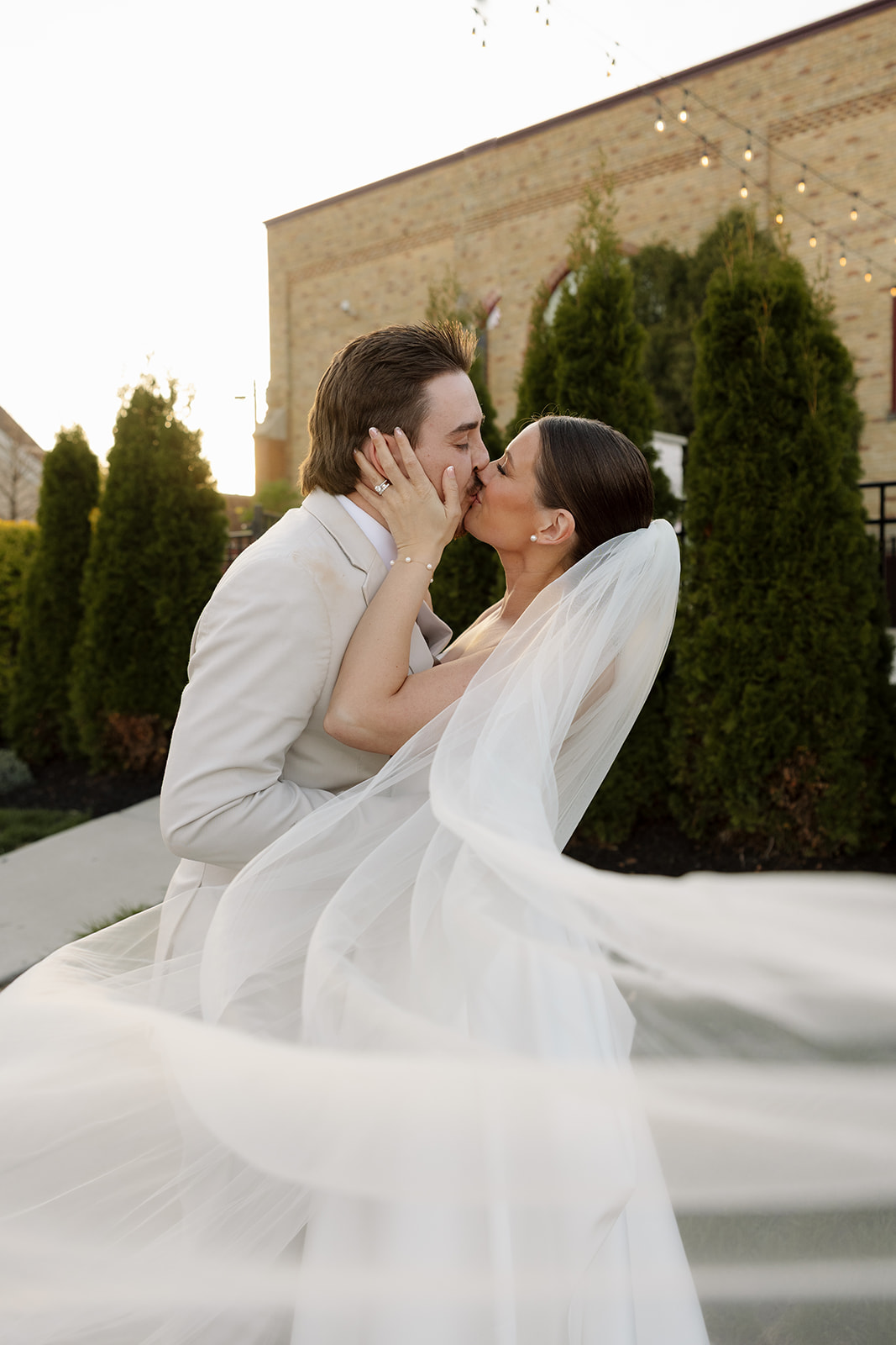 Bride and groom share a romantic kiss as her veil flows dramatically in the breeze at 10 South in Janesville, WI.