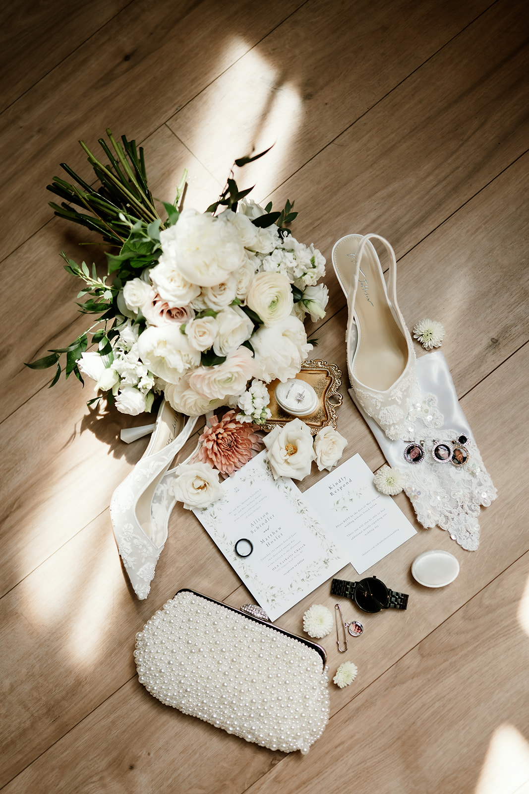 Flat lay of elegant bridal details including white bouquet, satin shoes, vow books, pearl clutch, heirloom pins, and floral accents.