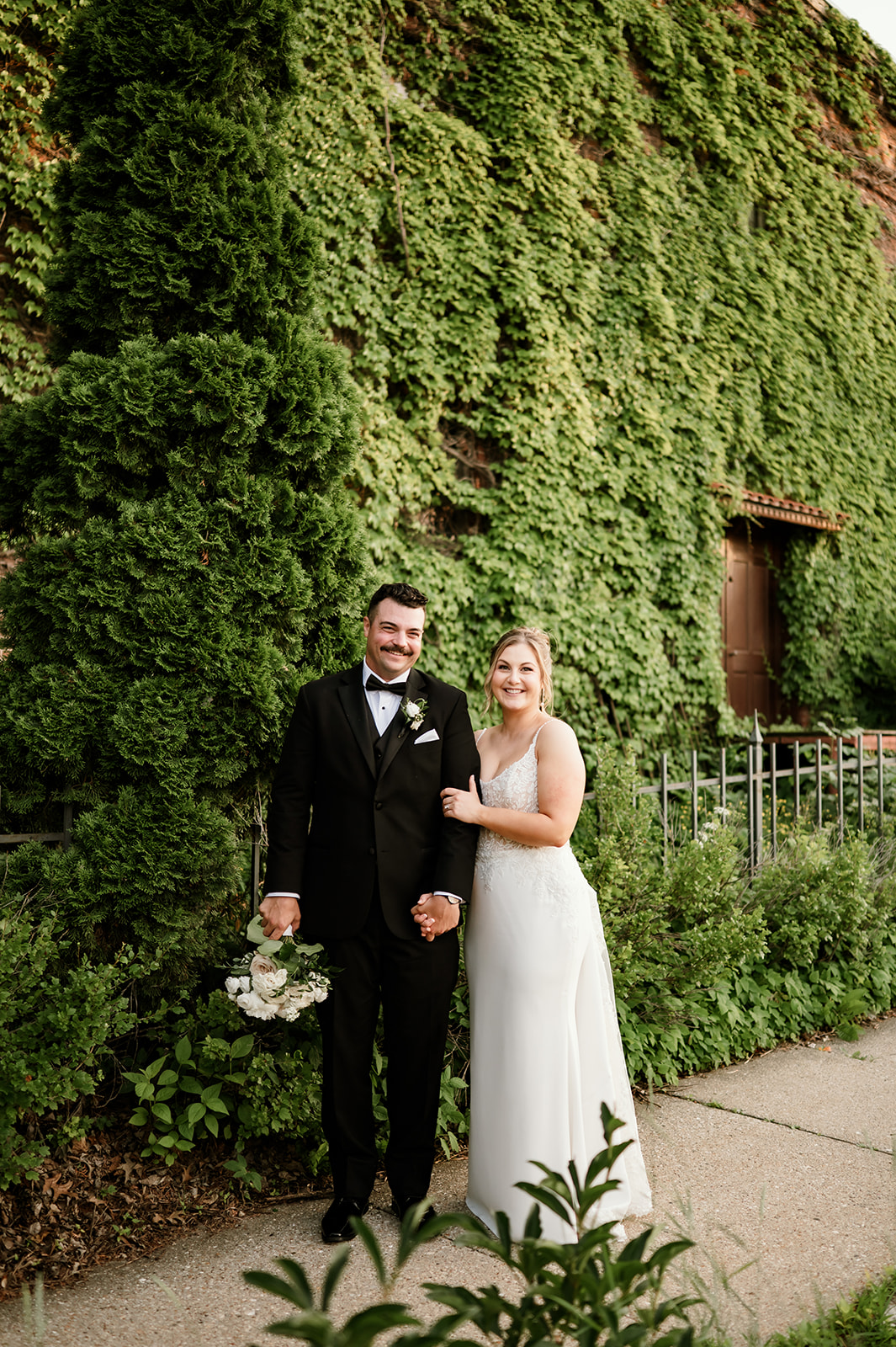 Bride and groom pose for a wedding portrait in front of an ivy-covered brick wall at 10 South in Janesville, Wisconsin.