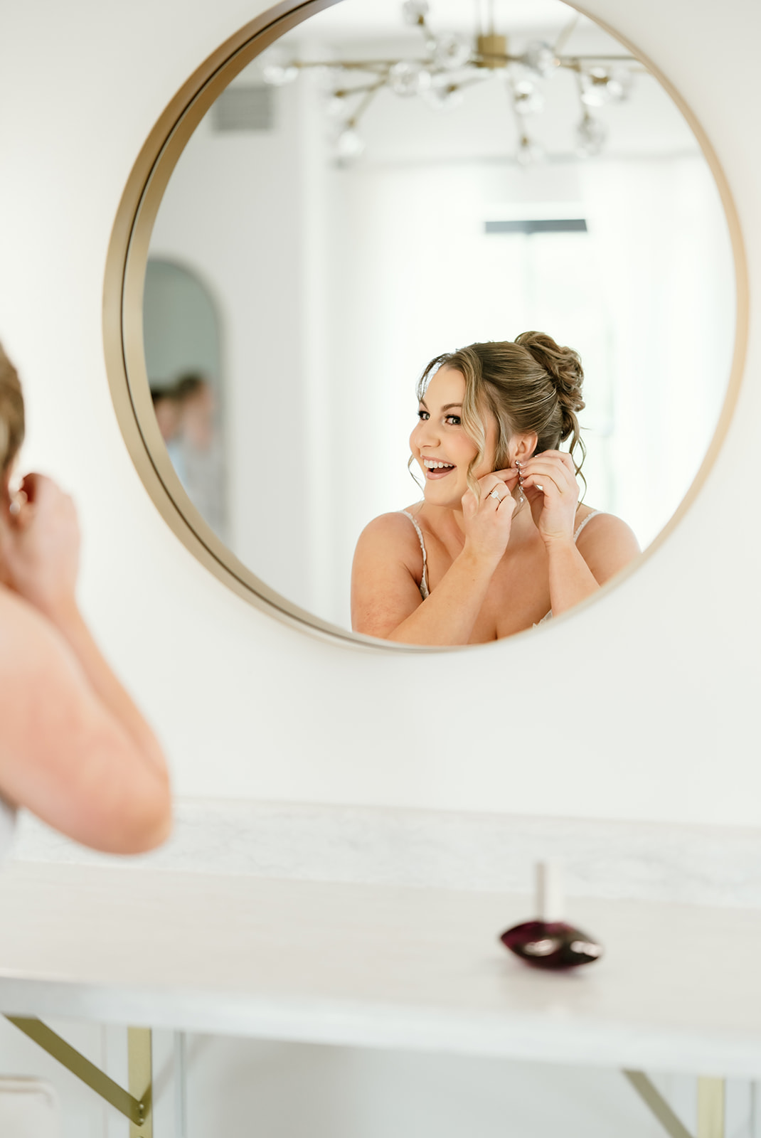 Bride smiles while putting on earrings in bridal suite mirror at 10 South wedding venue.