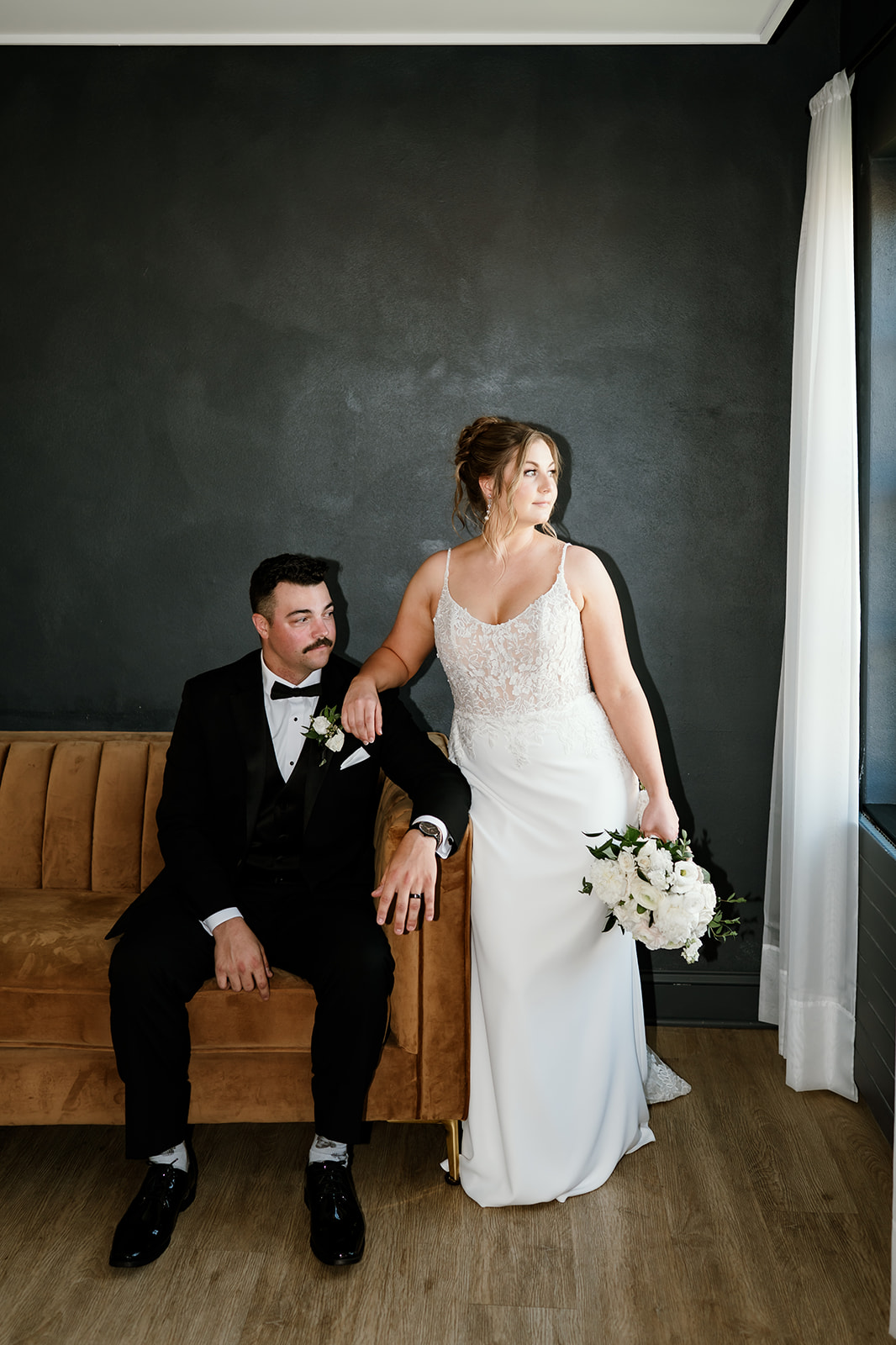 Bride and groom pose together in modern wedding suite with moody black wall and natural light at 10 South.