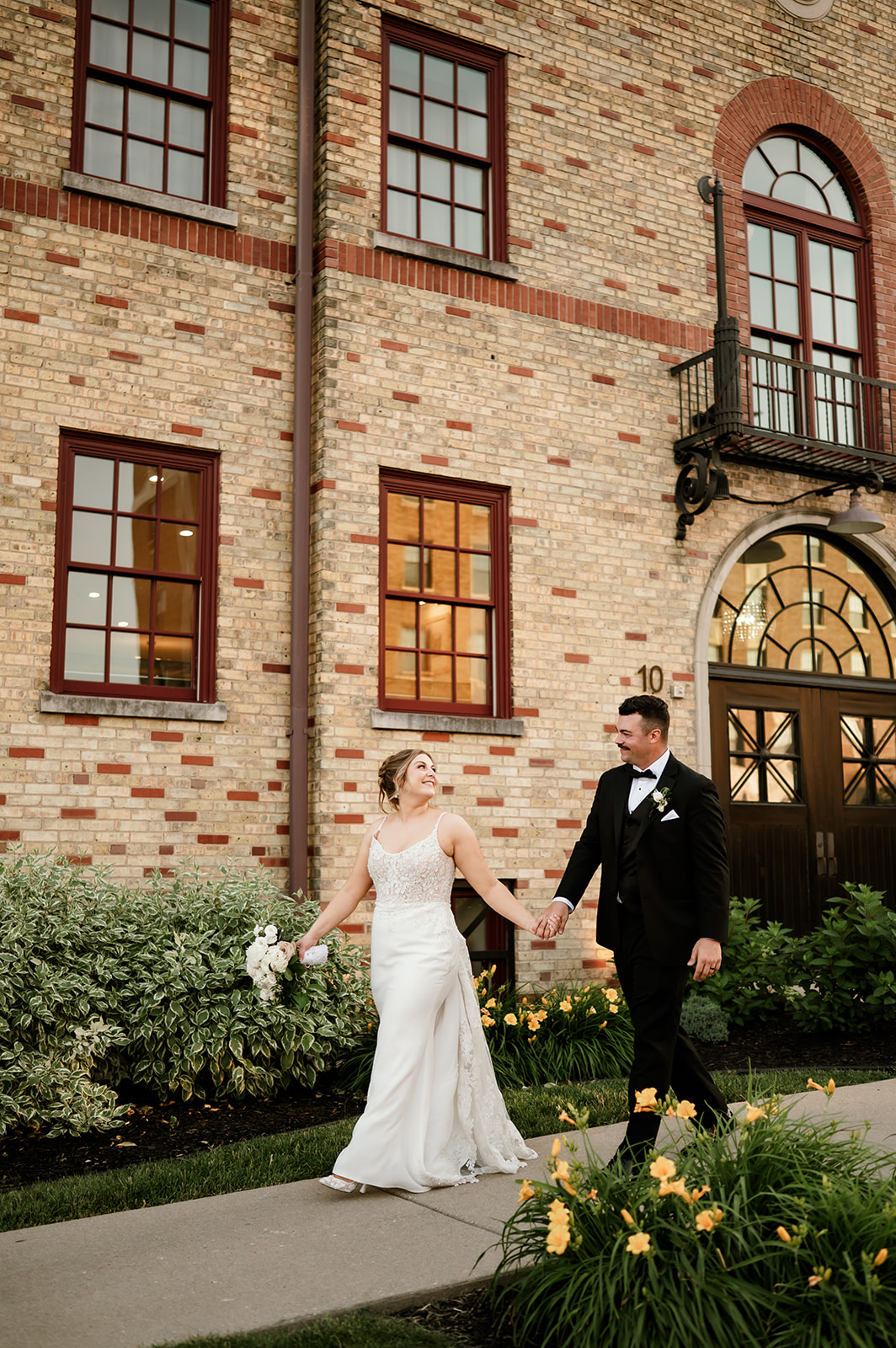 Bride and groom walk hand in hand in front of 10 South’s historic brick building in Janesville, Wisconsin.